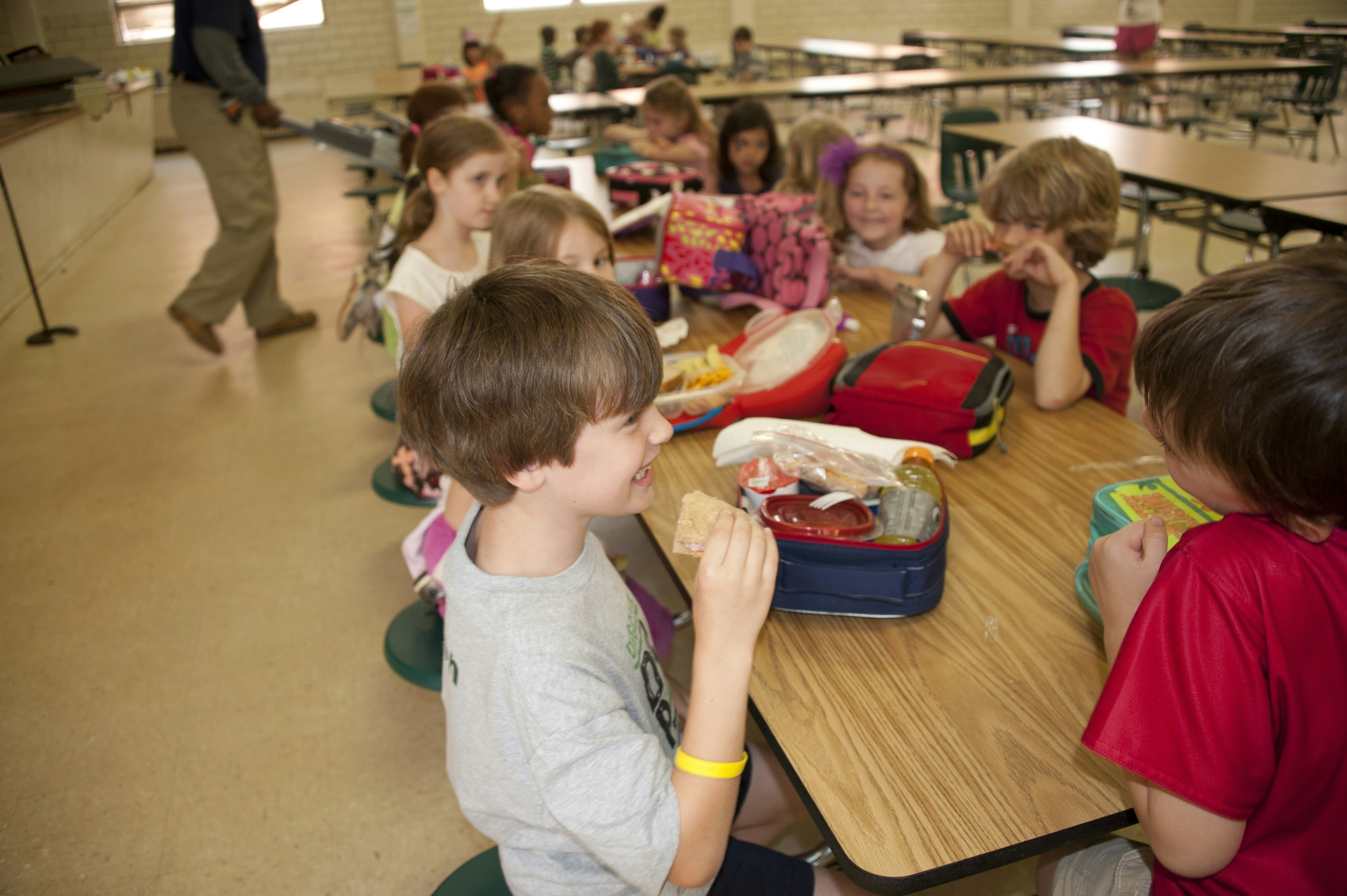 This image depicts a group of school children, who were seated in the lunchroom of a metropolitan Atlanta, Georgia primary school taking their daily lunch break during their school day activities. In this particular view, seated in the foreground, were two playful boys, one of whom was about to begin eating his whole-wheat sandwich, minus the crust. Hopefully, his lunch included some fresh fruit, as was the case for some of his classmates